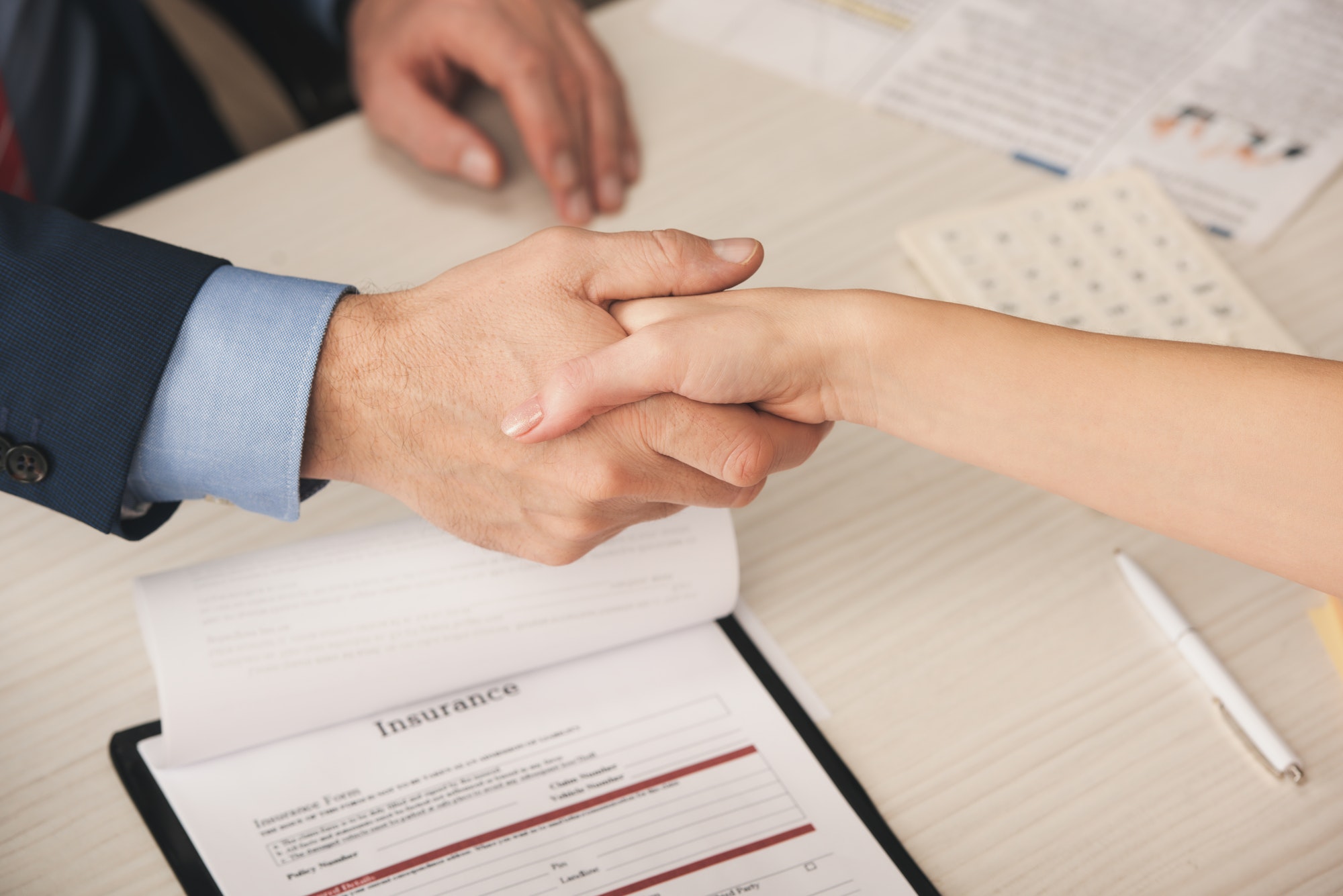 cropped view of agent and client shaking hands near clipboard with insurance lettering